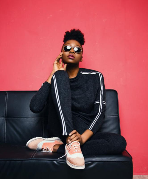 Girl in shades wearing a black tracksuit and sitting on a sofa.