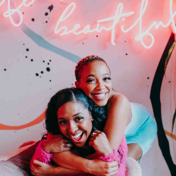 Two black women smiling and hugging each other.