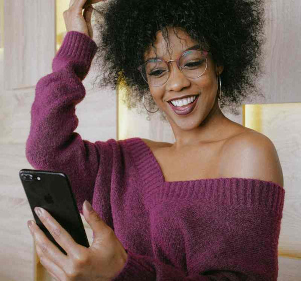 Black woman fixing her hair while looking at her cellphone.