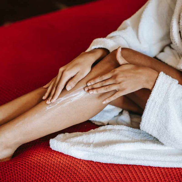 Girl in a bathrobe applying lotion on her legs.