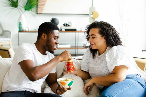 Black couple sitting on the couch and eating snacks.