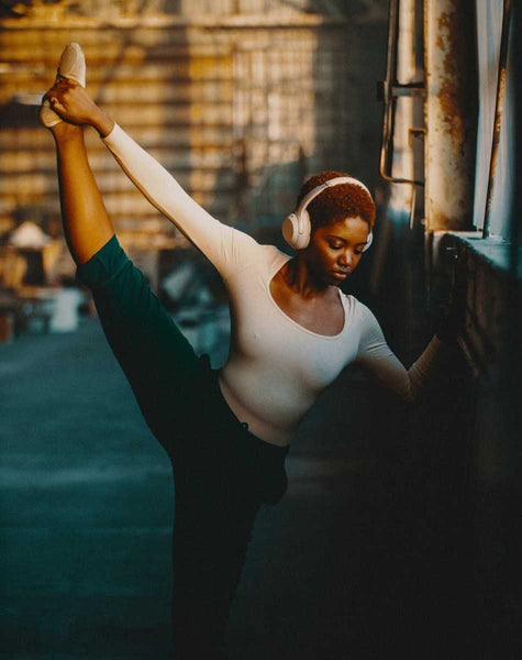Black ballerina with headphones on doing a leg stretch.
