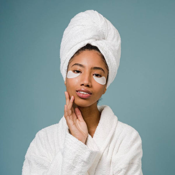 Girl in a bathrobe with towel in her hair and under-eye mask.