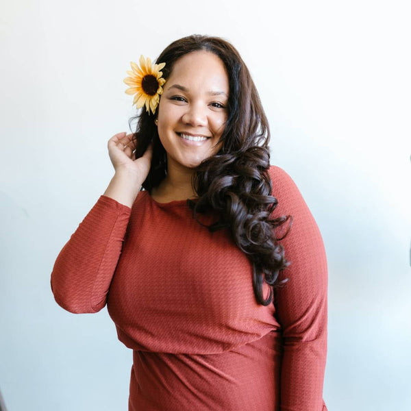 Black curvy girl wearing a red dress and posing with a sunflower on her ear.