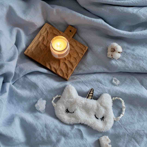 Unicorn sleep mask and candle on a bed.