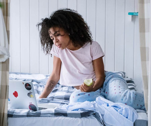 Black girl sitting in bed holding an apple wearing pajamas.