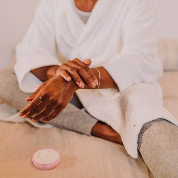 Black woman putting moisturizing cream on her arm.