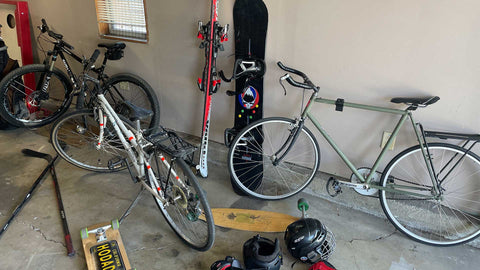 Garage cleanup with bikes, skis, a snowboard, helmets, and a skateboard laying on the ground.