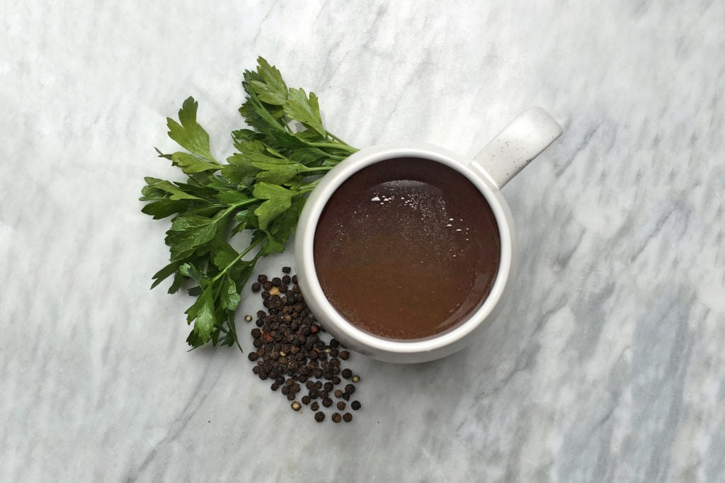 A flat lay of a mug of Pure Bone Broth next to parsley and peppercorns