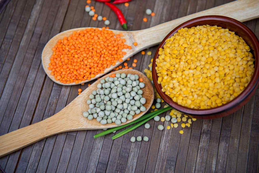 different colors of lentils on wooden spoons