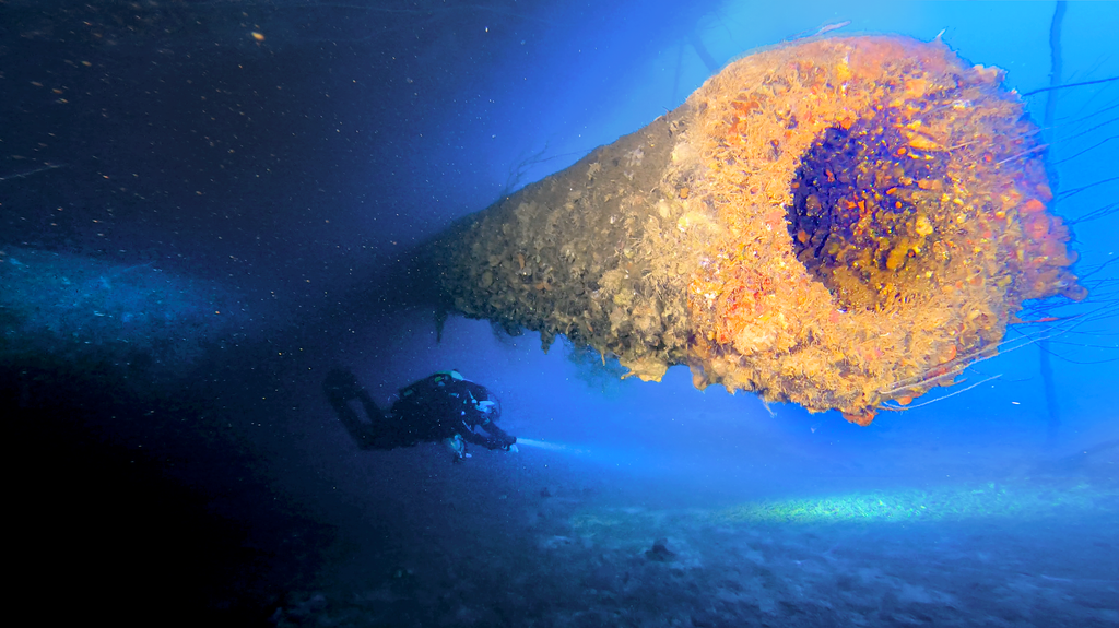 Close up of one of the 16 inch guns of the Nagato wreck in Bikini Atoll with diver beneath