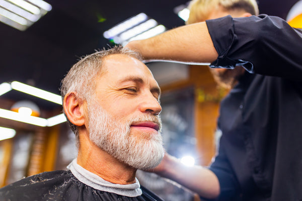 An elderly man with his eyes closed getting hair cut