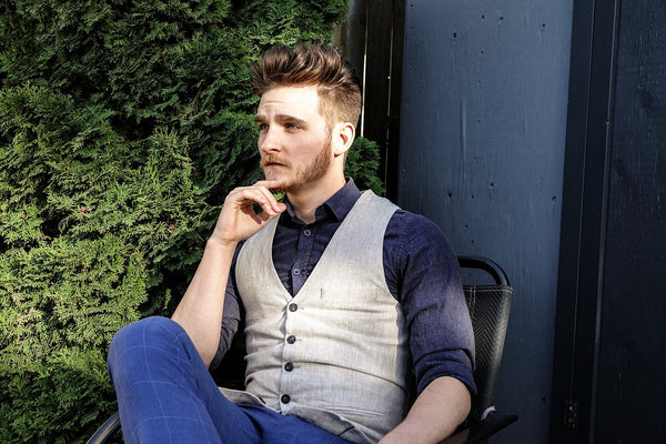 A man posing on a chair outside in a jacket and styled hair