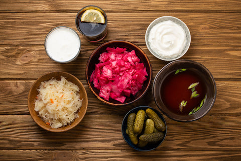 Top view of assorted fermented foods and drinks, sources of probiotics great for healthy gut and digestive system: kimchi, pickles, sauerkraut, miso soup, kombucha, yogurt, kefir, wooden background