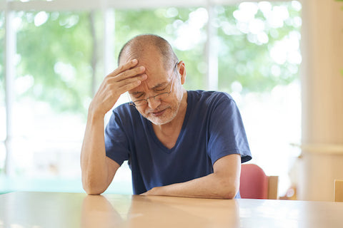 older adult man sitting at table with headache