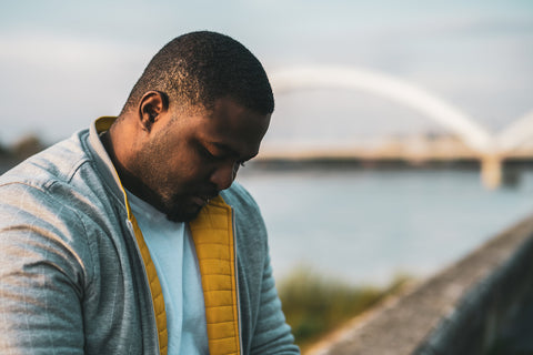 photo of a man sitting by the water looking depressed