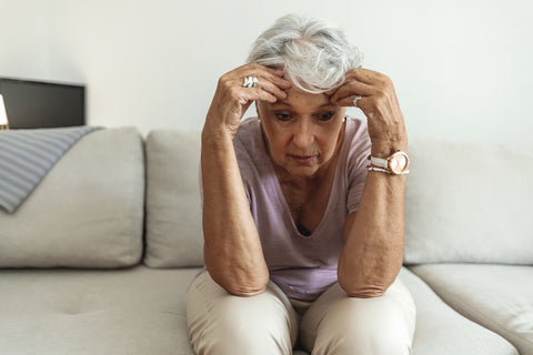 Pensive thoughtful senior lady holding head sitting on couch, memory and focus problems