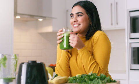 Happy woman drinking organic detox juice for her raw food diet from blender