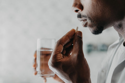 man holding glass of water about to take capsule