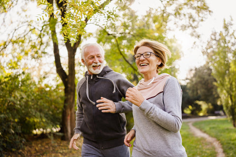 photo of older couple smiling and running in the park; longevity concept