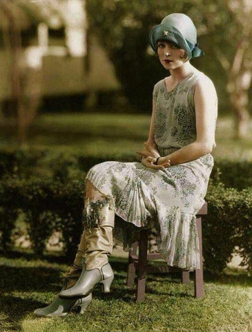 1920s silent movie star Clara Bow sits outside on a chair looking into the camera