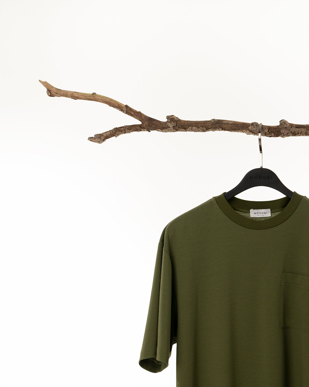Green T-shirt hanging from a tree branch with a hanger