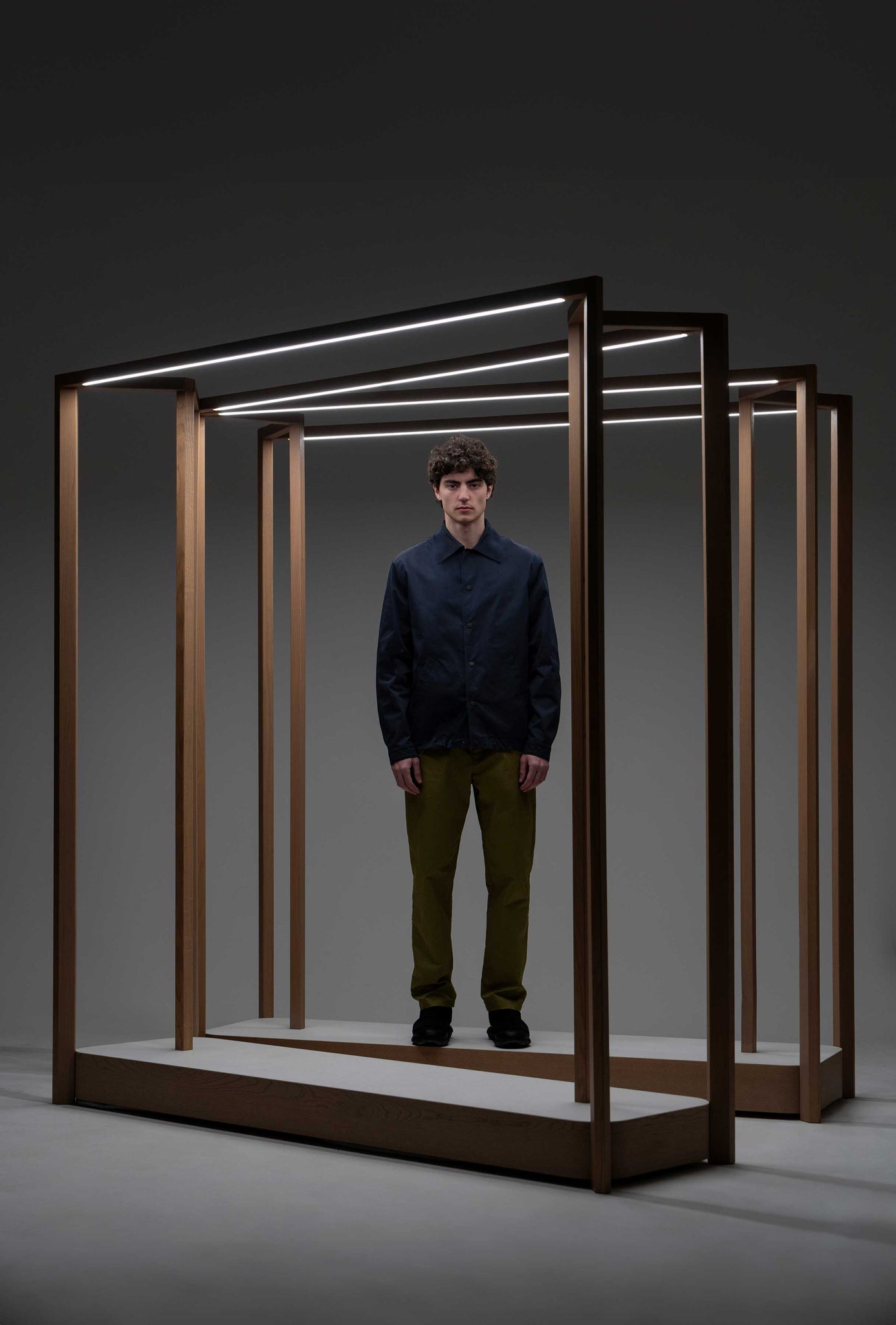 The model is in a wooden frame and wears a blue shirt and green cotton trousers