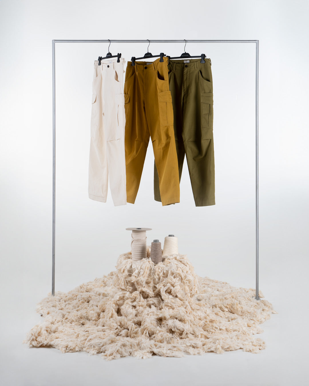 Three pairs of hanging cargo pants in three different colours: ochre, frog green and natural