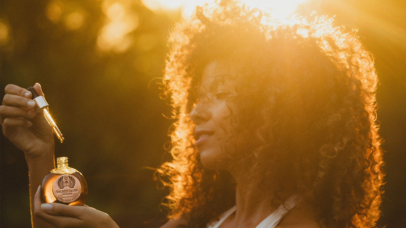 Woman holding a serum bottle with sunlight illuminating her curly hair.