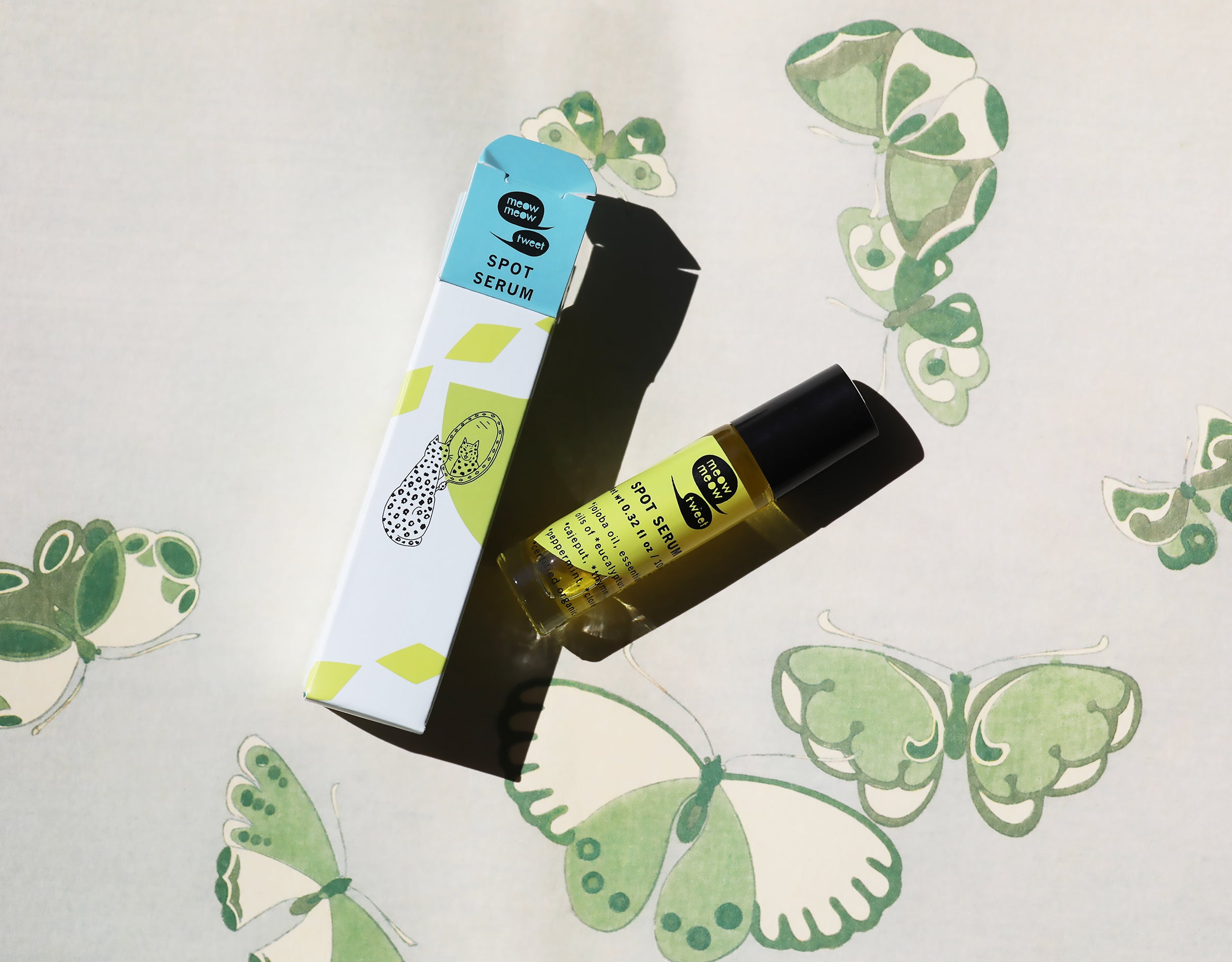 A bright closeup photo of our Spot Serum set against a green and white patterned butterfly background. 