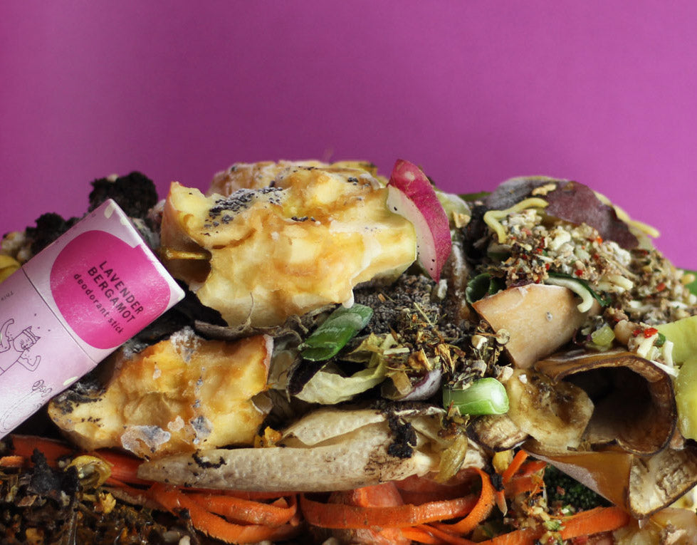 a pile of compost with a paper deodorant tube sits against a purple background
