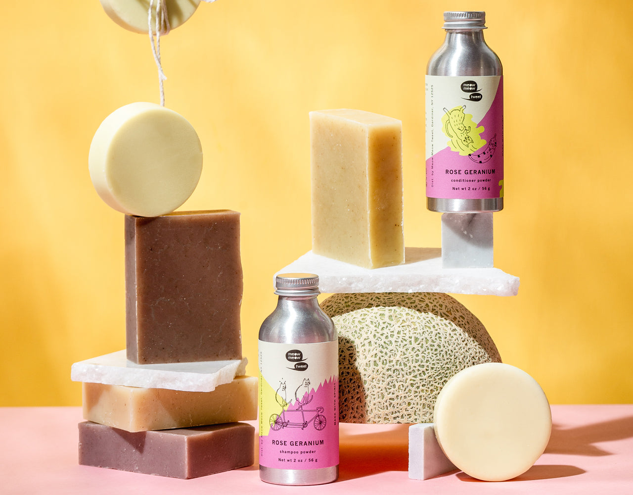 our hair bars and powders stacked in varying levels with slabs of marble and a cantaloupe. the background is peach and the ground is pink.
