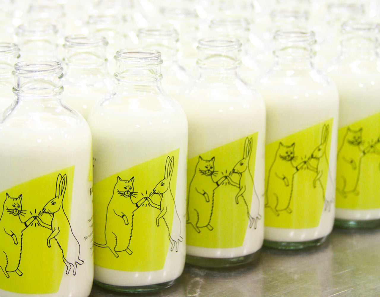 cream cleansers waiting in rows after being filled to be capped. the drawing on the bottle is a cat high-fiving a rabbit.