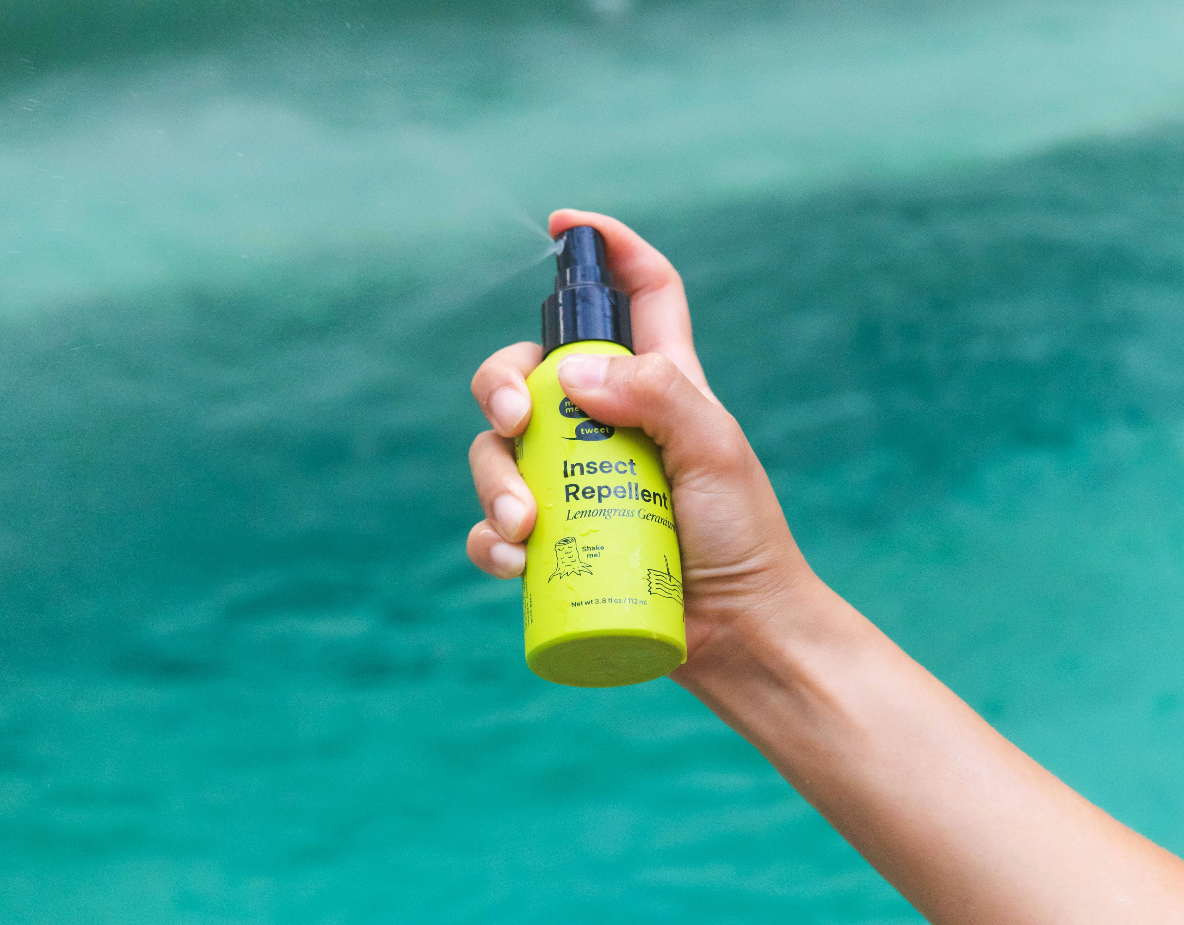 A green bottle is being spritzed by a light brown hand over a turquoise swimming pool