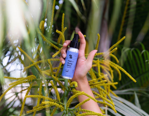 A blue bottle held by a light brown hand in front of some plant fronds