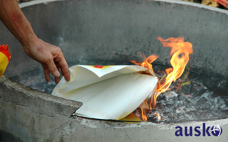 a person placing joss paper with one hand in the incense burner