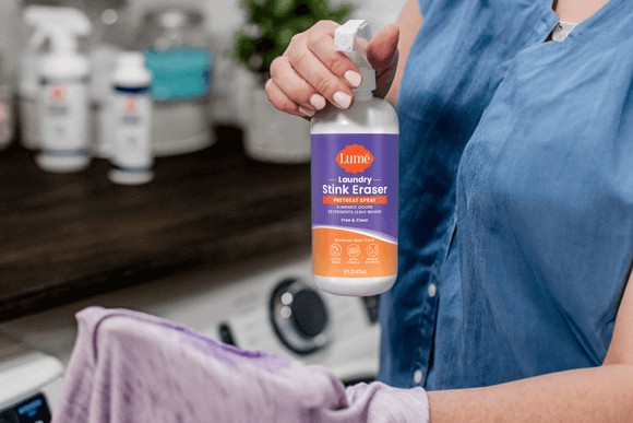 A woman using the Laundry Stink Eraser Pretreat Spray on the inside seam of a shirt