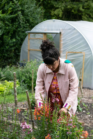 Sarah picks flowers with the cutting garden in the distance. Sarah of We Grow Colour wears Humphries and Begg pink embroidered jacket