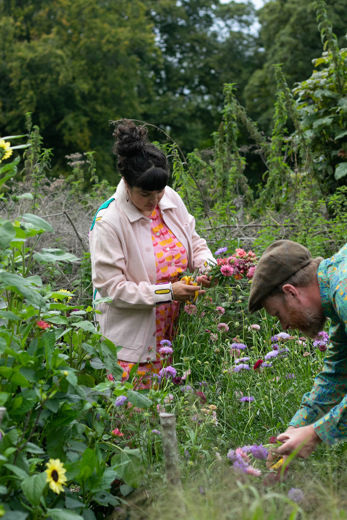 Sarah and Rory in the garden picking cornflowers. Sarah wears Humphries and Begg pink embroidered jacket and Citrus segments dungarees