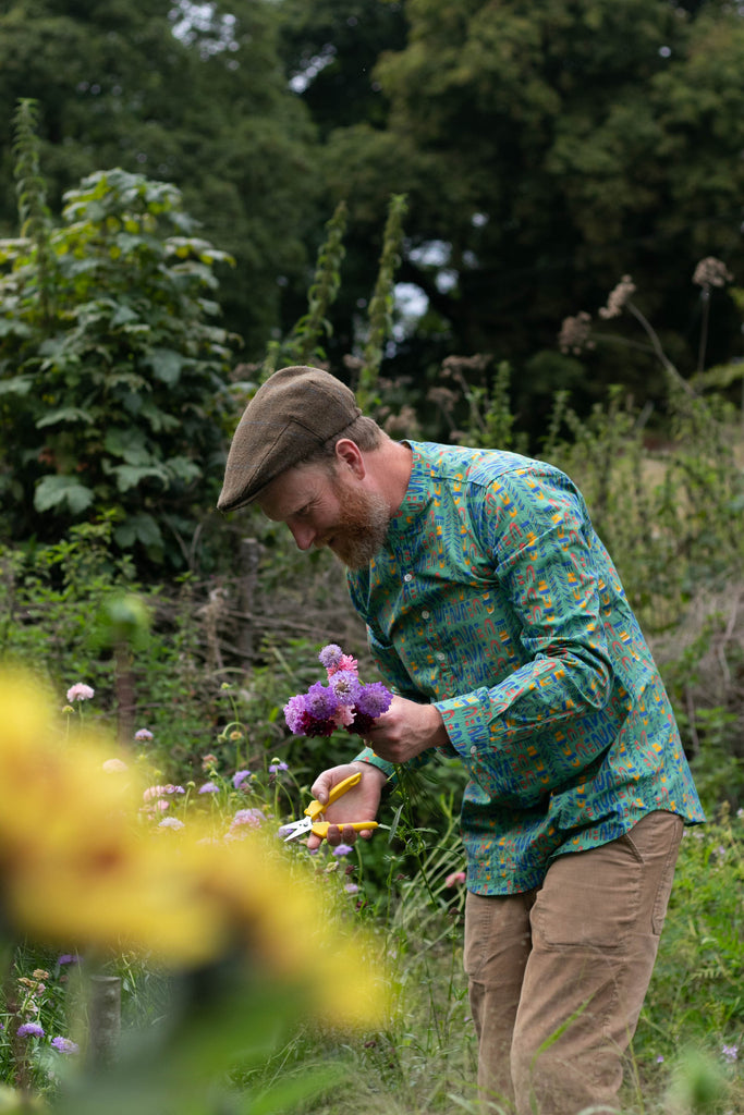 Rory Picks flowers in the garden in his green skydive shirt. 