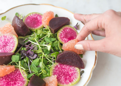 hand placing grapefruit and beets on salad