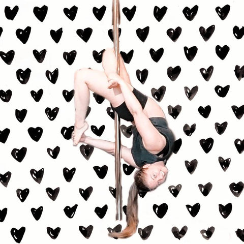 female pole dancer doing a layback pole move with an edited heart background