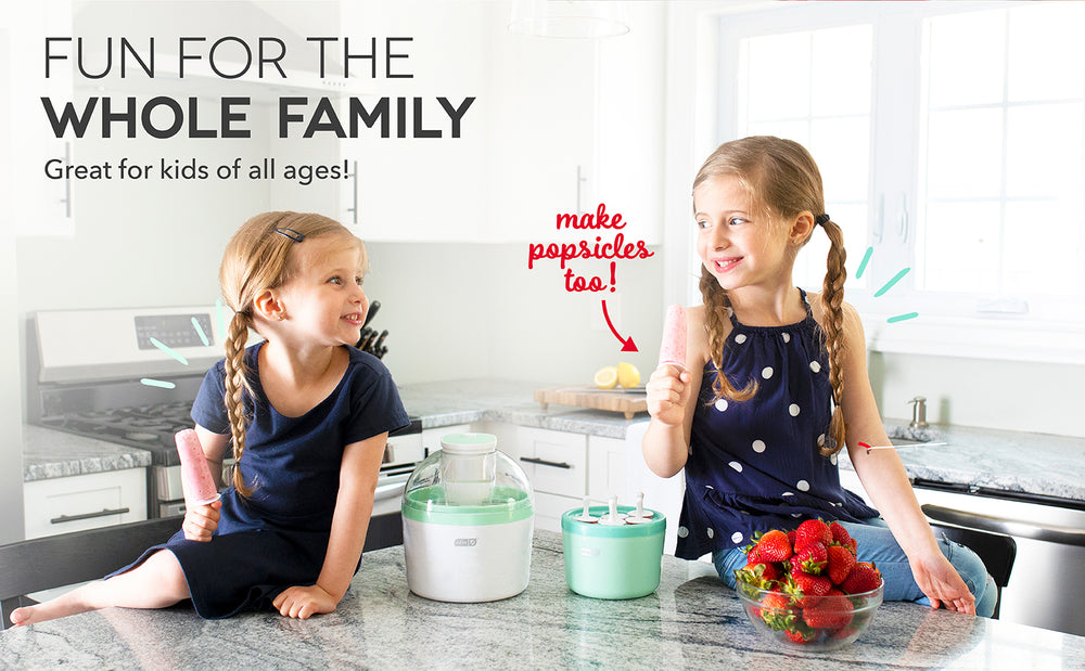 2 smiling girls in matching pigtail braids sit on a counter with a blue Everyday Ice Cream Maker between them.