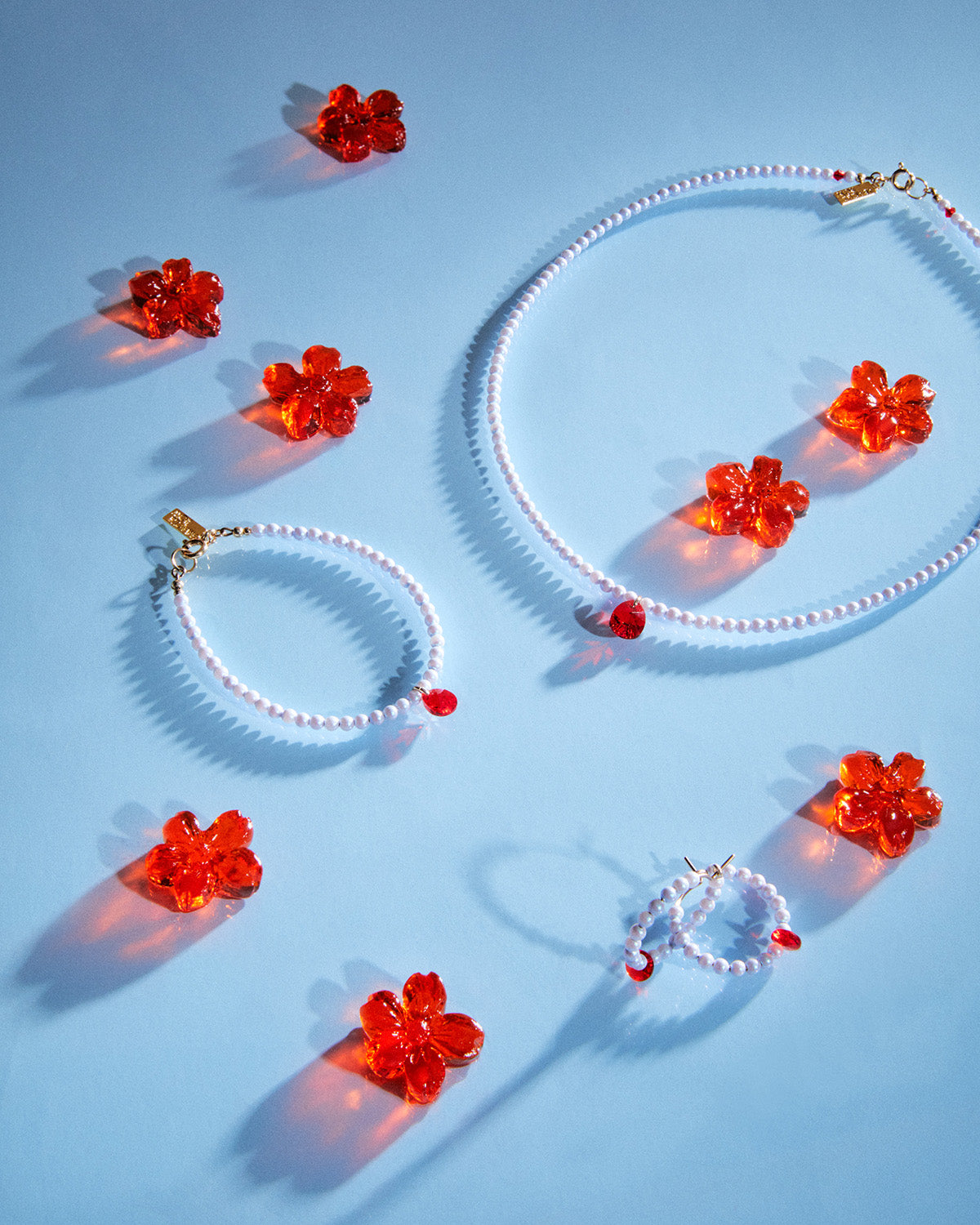 White Rabbit Collection (hoop earrings, necklace and bracelet) from the Water Moon Collection laid out on light blue surface with red translucent floral gelatins.