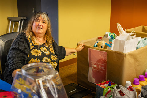Hostel Shoppe Marketing Manager, Jessie Bostic, sitting in front of a box of donations for the Women Helping Women Event.