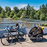 Mother and kids watch a stream with their bike and Burley Burley child trailer in the foreground.