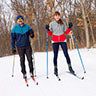 Man and woman cross country skiing in the snowy woods.