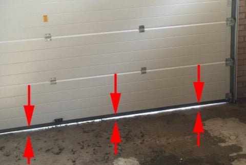 Arrows pointing to the space between the garage door and floor showing a gap