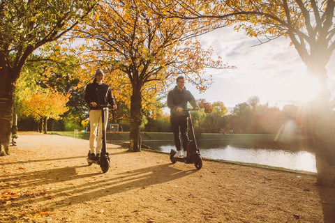 man and woman riding electric scooters in autumn