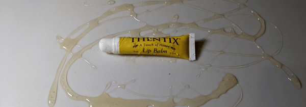 Thentix lip balm on a white surface covered in honey.